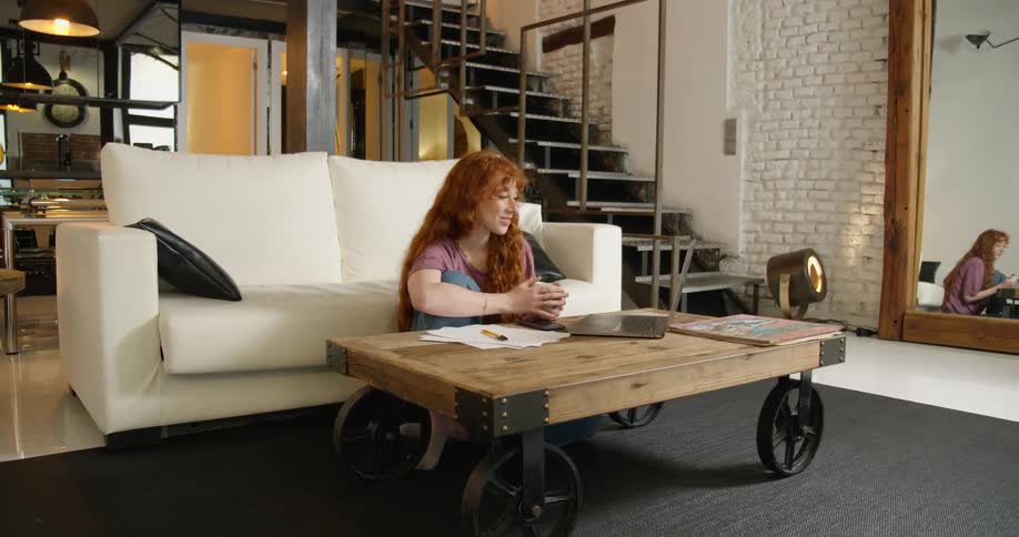 Young ginger woman talking on a video conference from the living room
