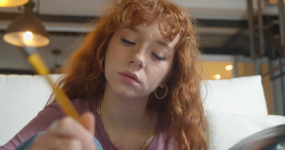 A woman with earrings in a room holding a pen with a wall in the background