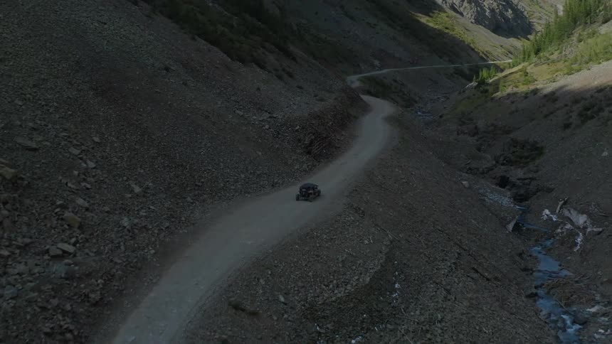 A vehicle driving on a dirt road next to a stream with trees and plants in the background