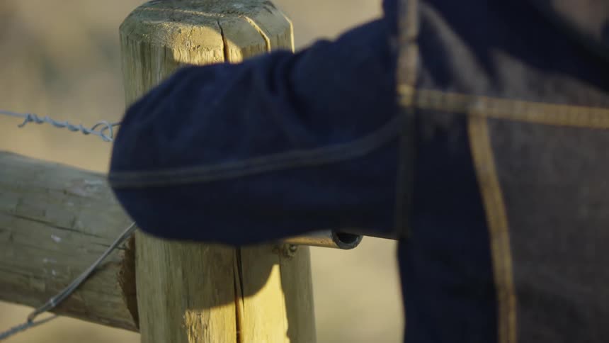A young rancher mends fence while closing a gate deep in the mountains of Montana