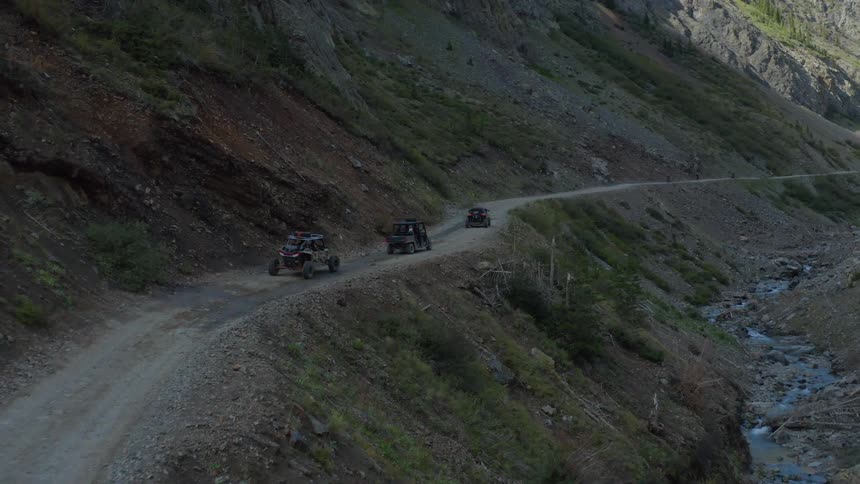 Three dune buggies drive a tight dirt road along a mountainside