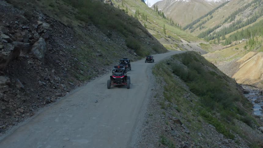 A group of dune buggies travel a gravel road along side a mountain
