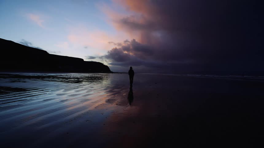 Man walking over the wet sand near the ocean at sunset