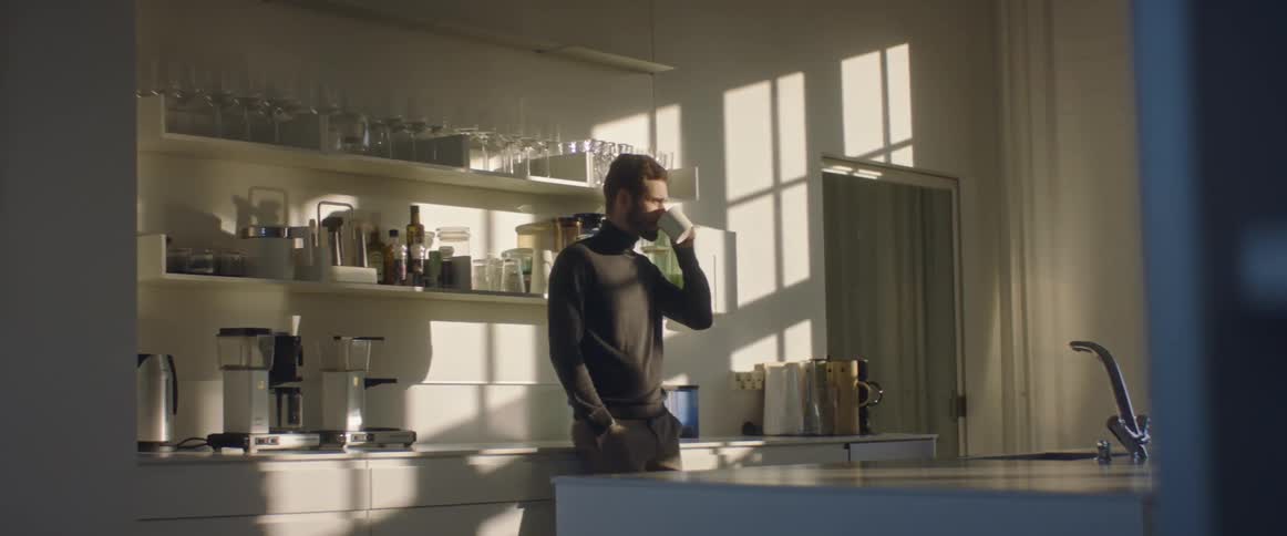 A man drinking coffee out of a mug in a kitchen