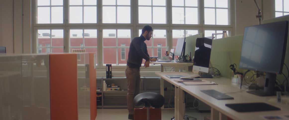 A man in an office stands at a work station and uses a computer