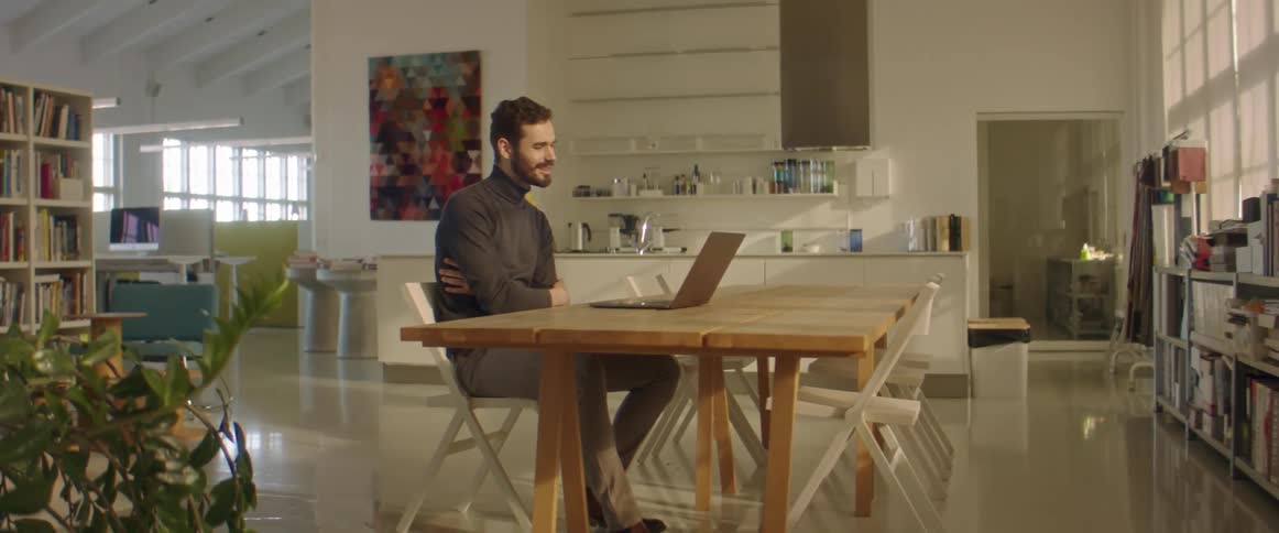 Man talks while sitting at a table looking at a laptop