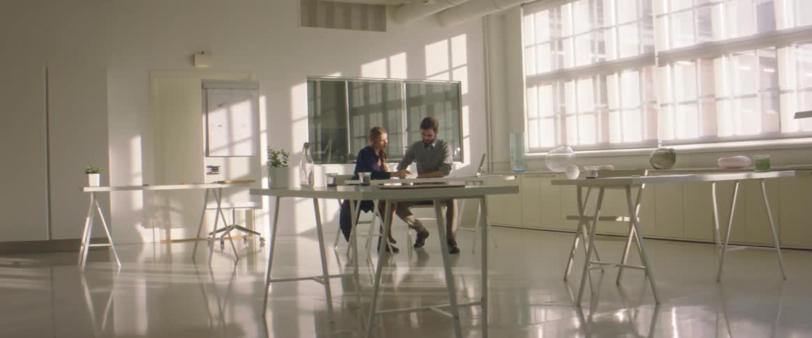 Two coworkers sit at table in room having a discussion