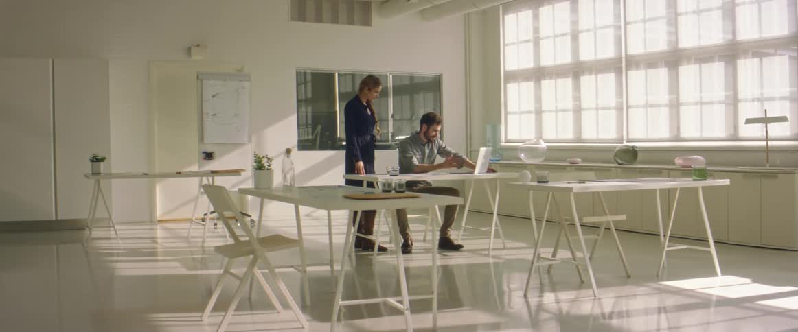 A man and a woman in a room looking at a laptop with a wall in the background
