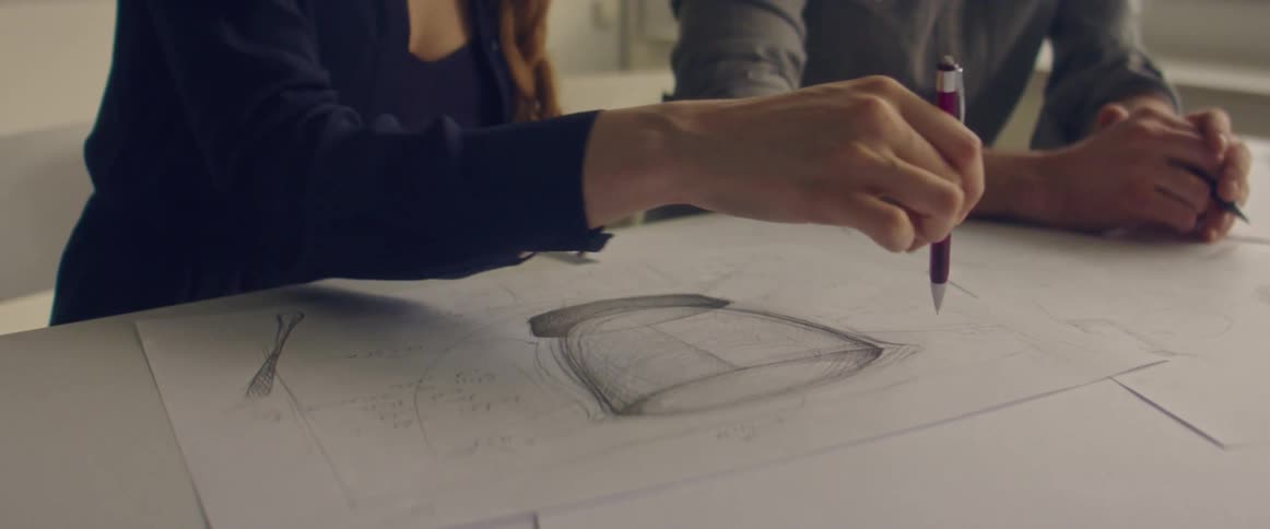 Two people in a room sitting at a desk holding pens and looking at a piece of paper