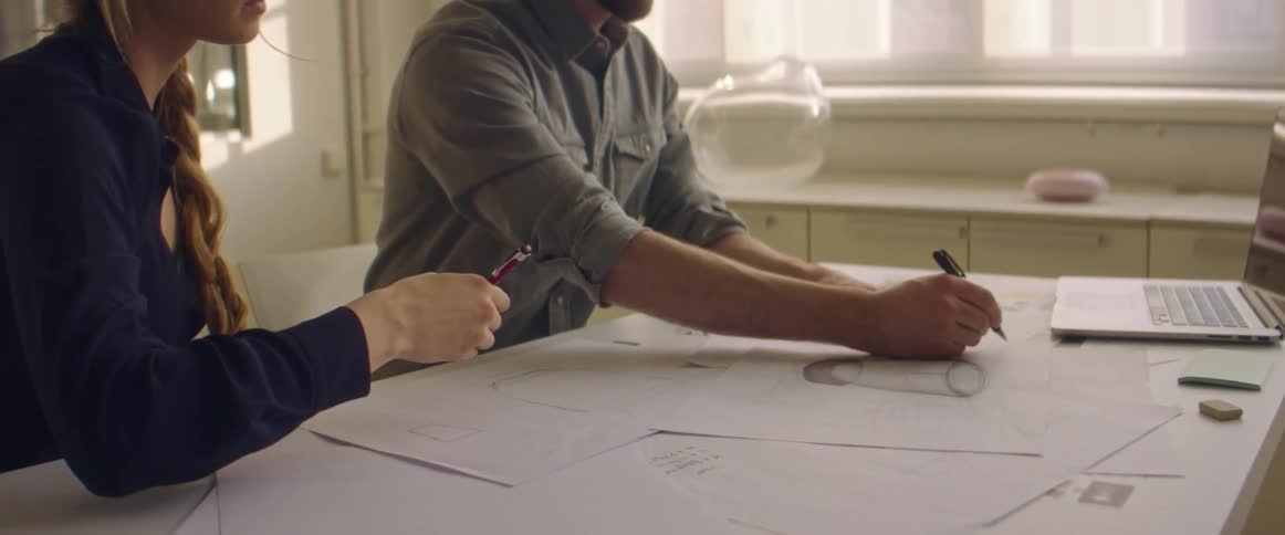 Two workers draw on diagram while sitting at table
