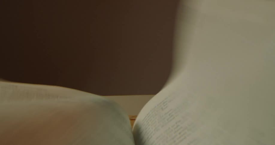 A book in a room on a table with wind blowing the pages with a wall in the background