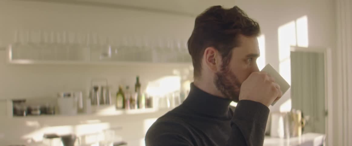 A man stands in a kitchen area drinking from a small mug