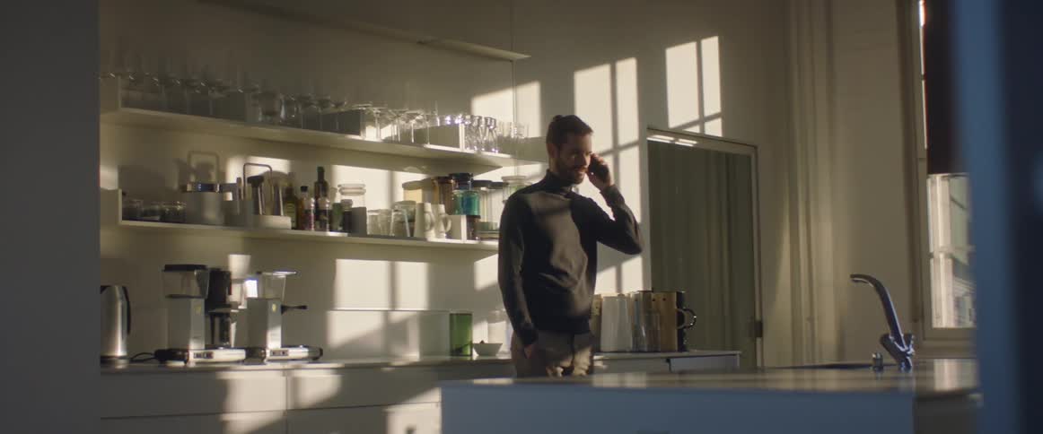 Bearded young man talking on the phone in the office kitchen