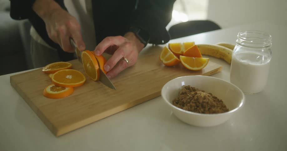 Person with a black shirt and a ring cuts orange on cutting board with a knife