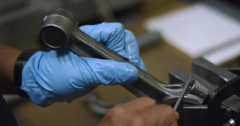 A person in a room with a glove filing a piece of metal
