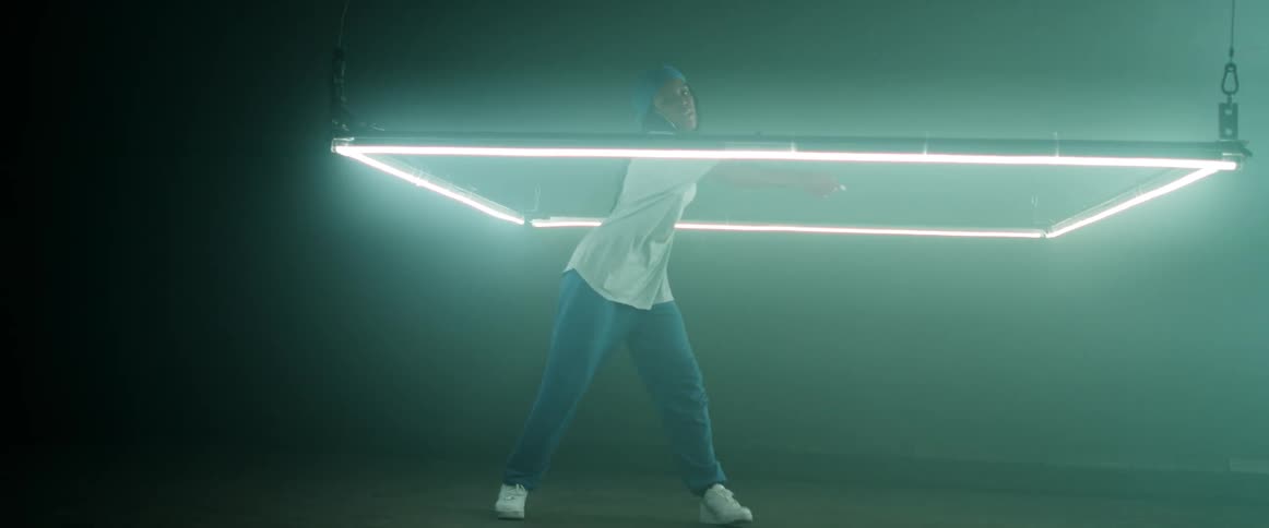 A dancer performs an unusual dance while standing within a low hanging rectangular light fixture
