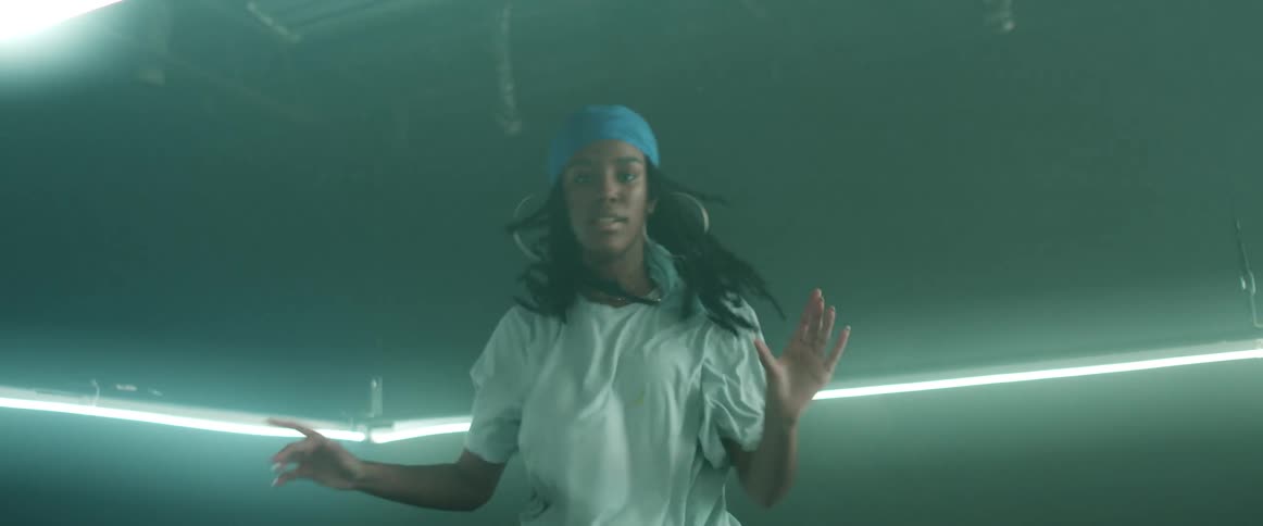 A girl with a bandanna and earrings dancing in a room