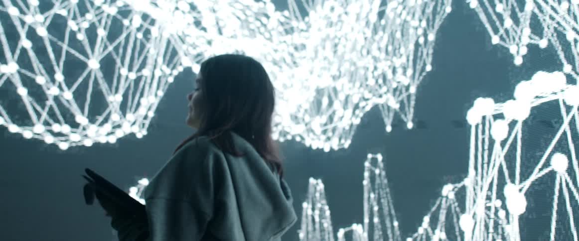 A woman in a hoodie using a tablet in a room with a screen in the background