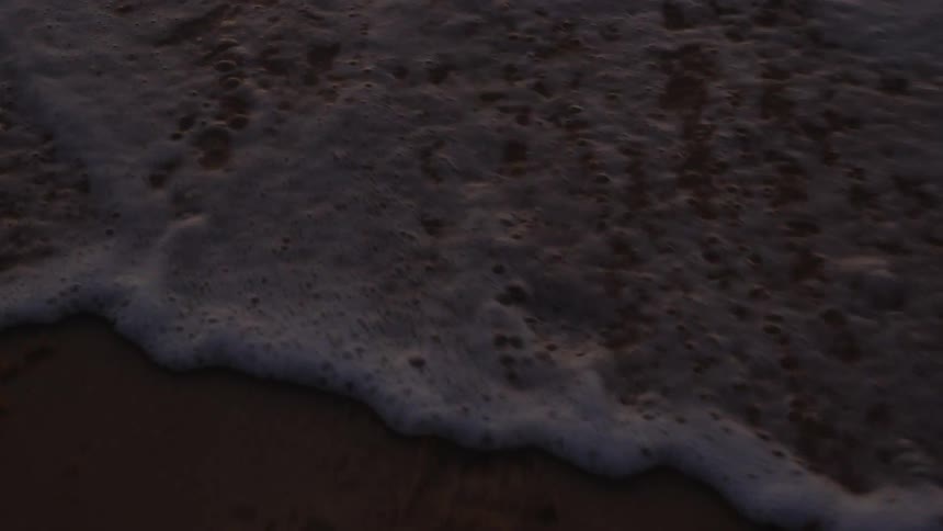 Small waves foaming over the sand on the coastline of a beach at evening