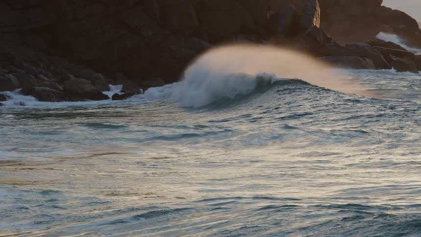An ocean wave crashes inwards towards a shore