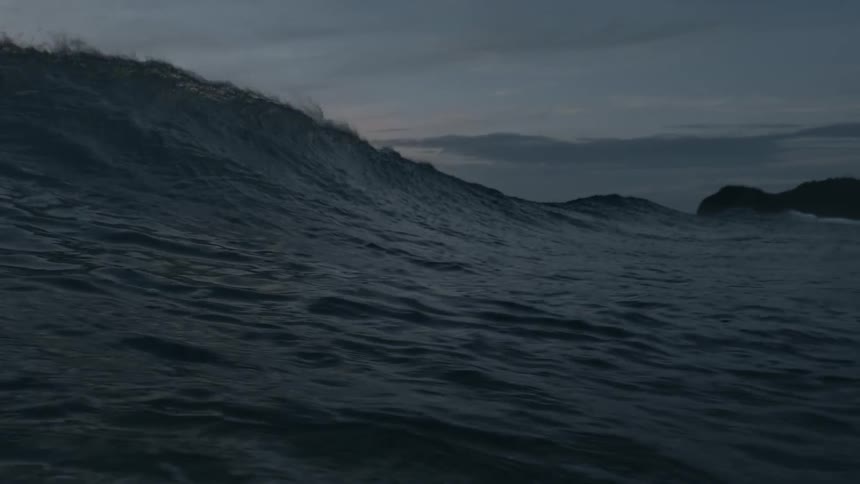 An ocean wave curls and breaks at sunset