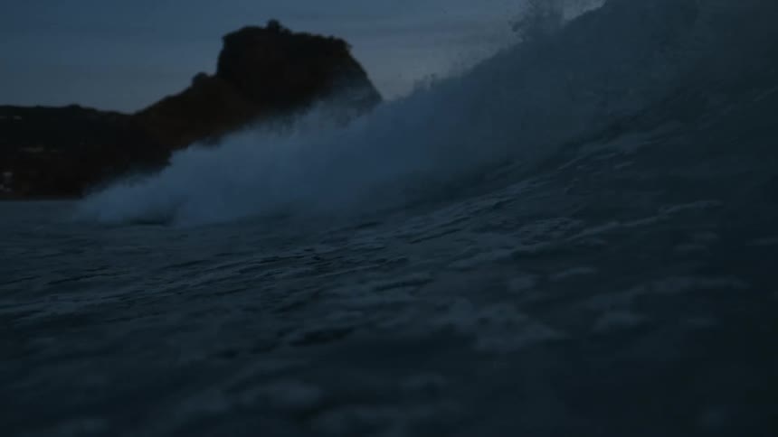 An ocean wave curls breaks and splashes at sunset