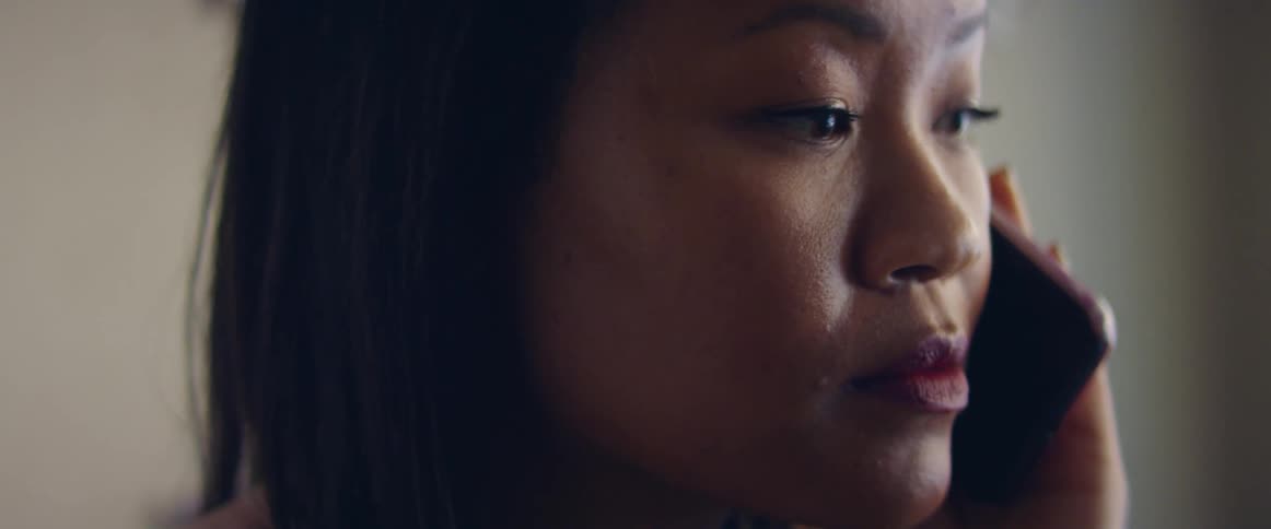 An asian woman holds her cell phone up to her ear and looks around while listening