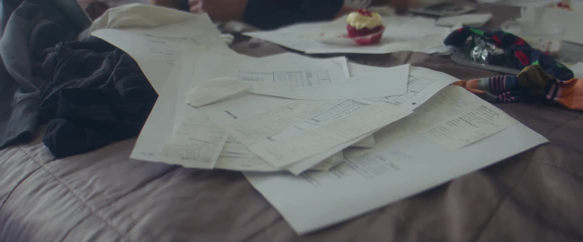 Person lies on bed near laptop cupcake and scattered paperwork
