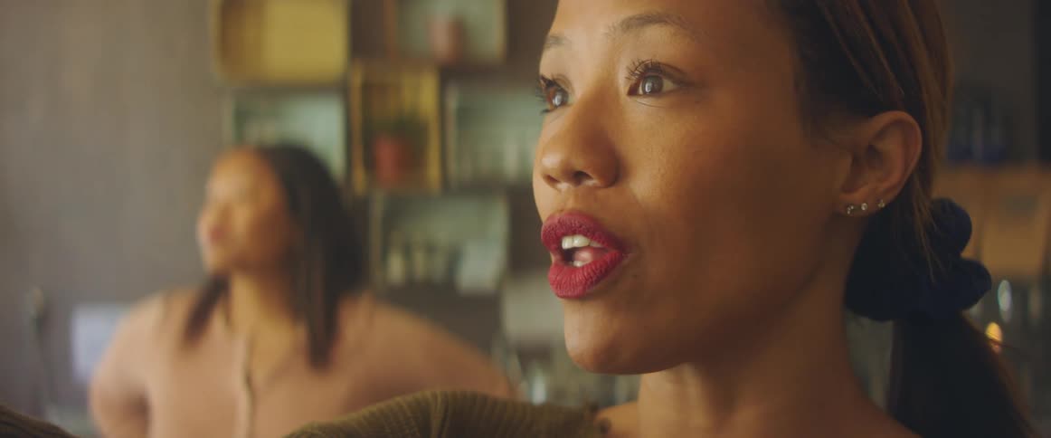 A woman gestures with her arm while speaking to another woman standing nearby indoors during the day