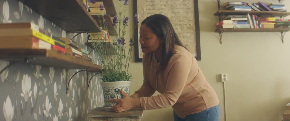 A woman in a room placing a potted plant on a table next to a wall with shelves