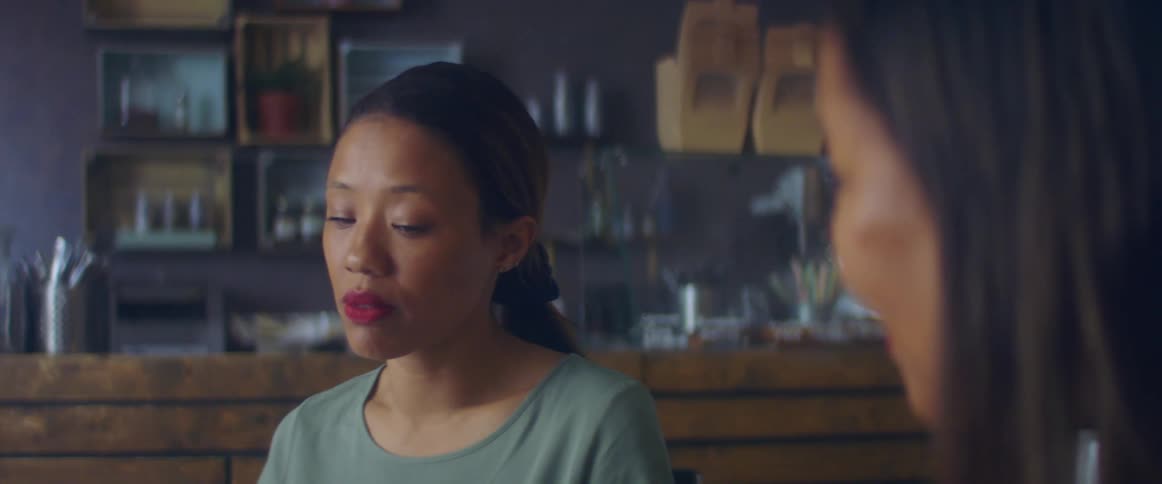 Sad looking woman with a grey sweater and a ponytail sits at table in the restaurant