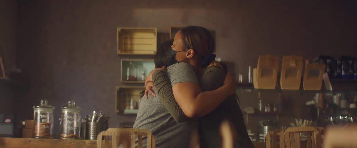 Two women in a room wearing mask with a wall and shelves in the background