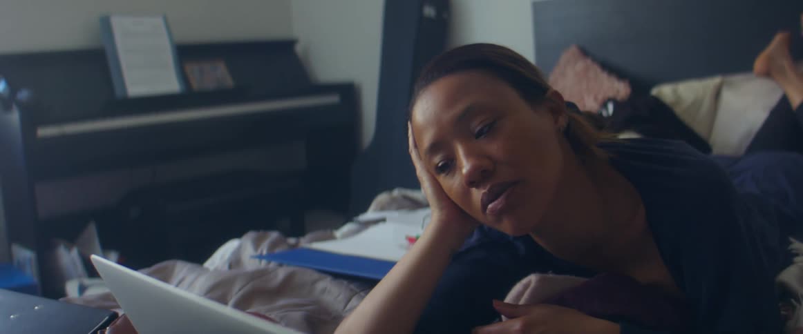 A teenage girl lies on her bed and looks at her laptop