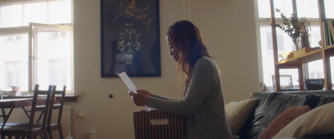 A woman sitting on a sofa removes a paper from a box on her lap and reads it