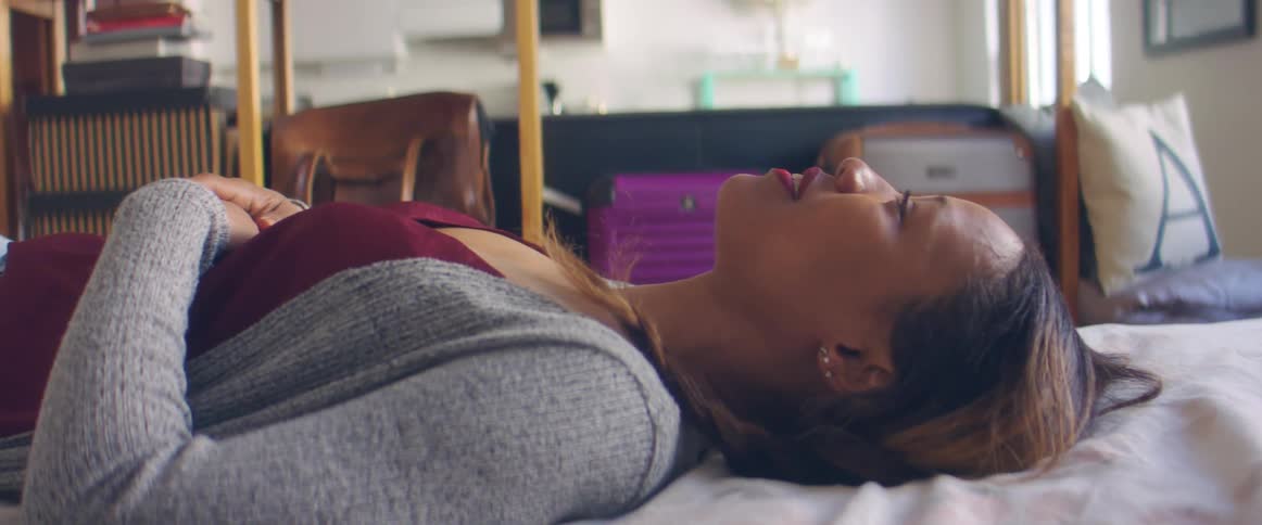 Woman wearing cardigan lies back on bed smiling