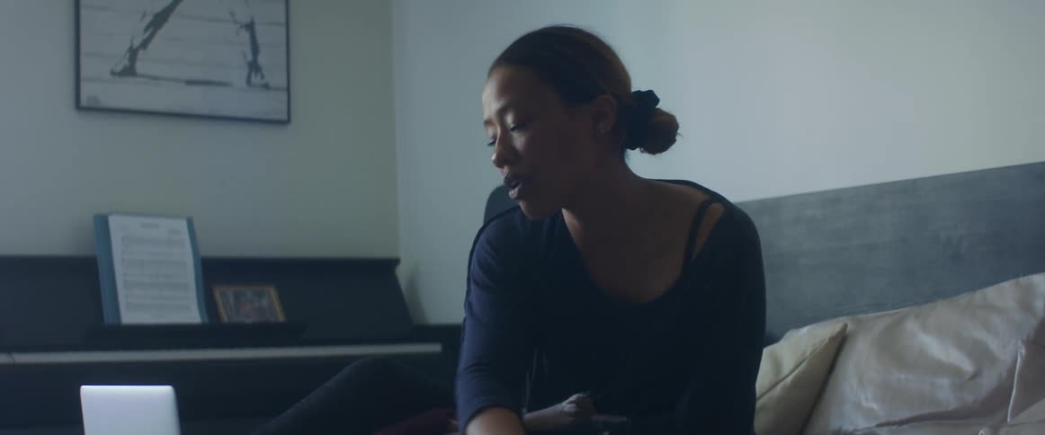 Woman with a dark blue shirt siting on bed uses a smartphone and closes her laptop in the bedroom
