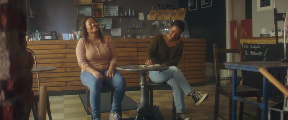 Two women sitting at table talk to each other in cafe shop