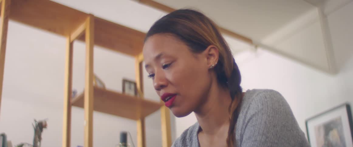 A woman in a room with a shelf a picture frame and a wall in the background