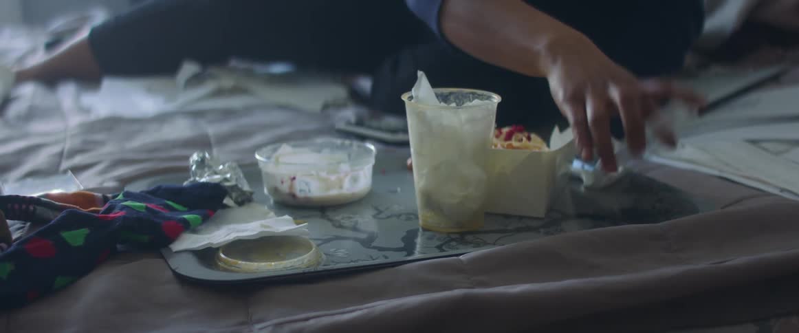 A person in a bedroom laying in bed cleaning up food on a tray