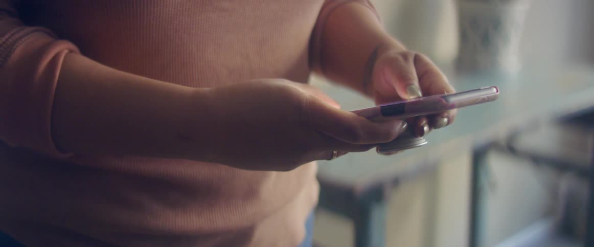 A person in a room using a smart phone with a wall and a window in the background