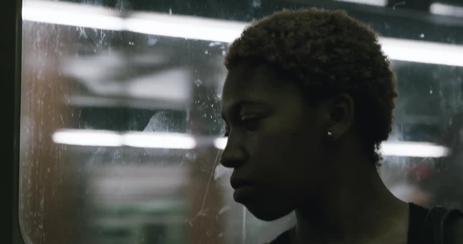 A woman is looking out the window as she rides the subway