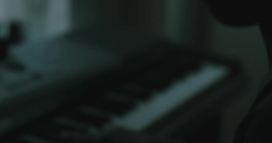 A woman in a room sitting and playing a keyboard with a wall in the background