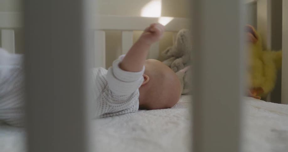 Baby lying on back in crib kicks feet and waves arms
