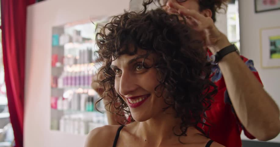 A man with glasses in a hair salon fixing a womans hair with a wall in the background