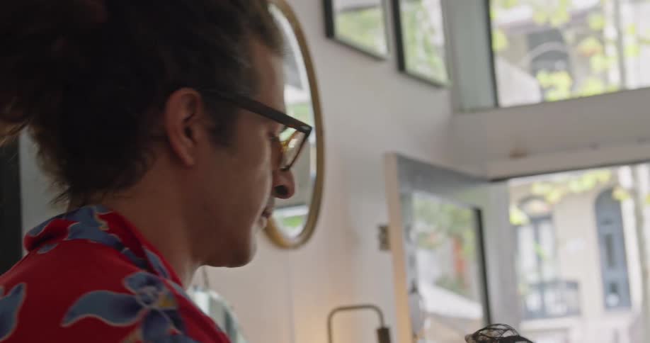 A man with glasses in a hair salon with a wall and a mirror in the background