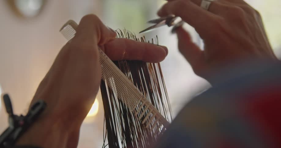 A hairstylist holds the hair of a customer run combs it before trimming it with scissors
