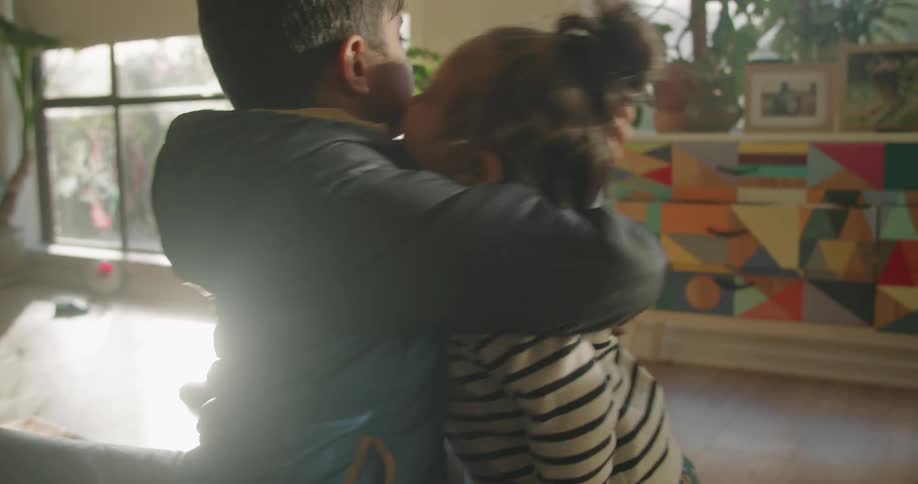 A little girl at home walks over to her brother and they hug