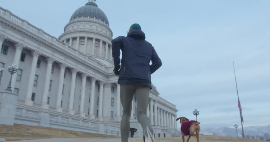 A man is jogging with his dog up a flight of stairs in a city