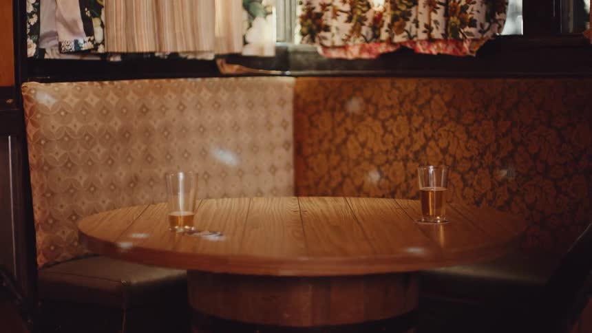 Swirling dots of light move over wooden table and two glasses of beer in corner booth under curtained window