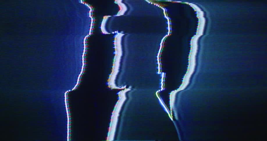 The silhouette of a man is seen as he stands in front of a large digital screen with distorted imagery and colors on it